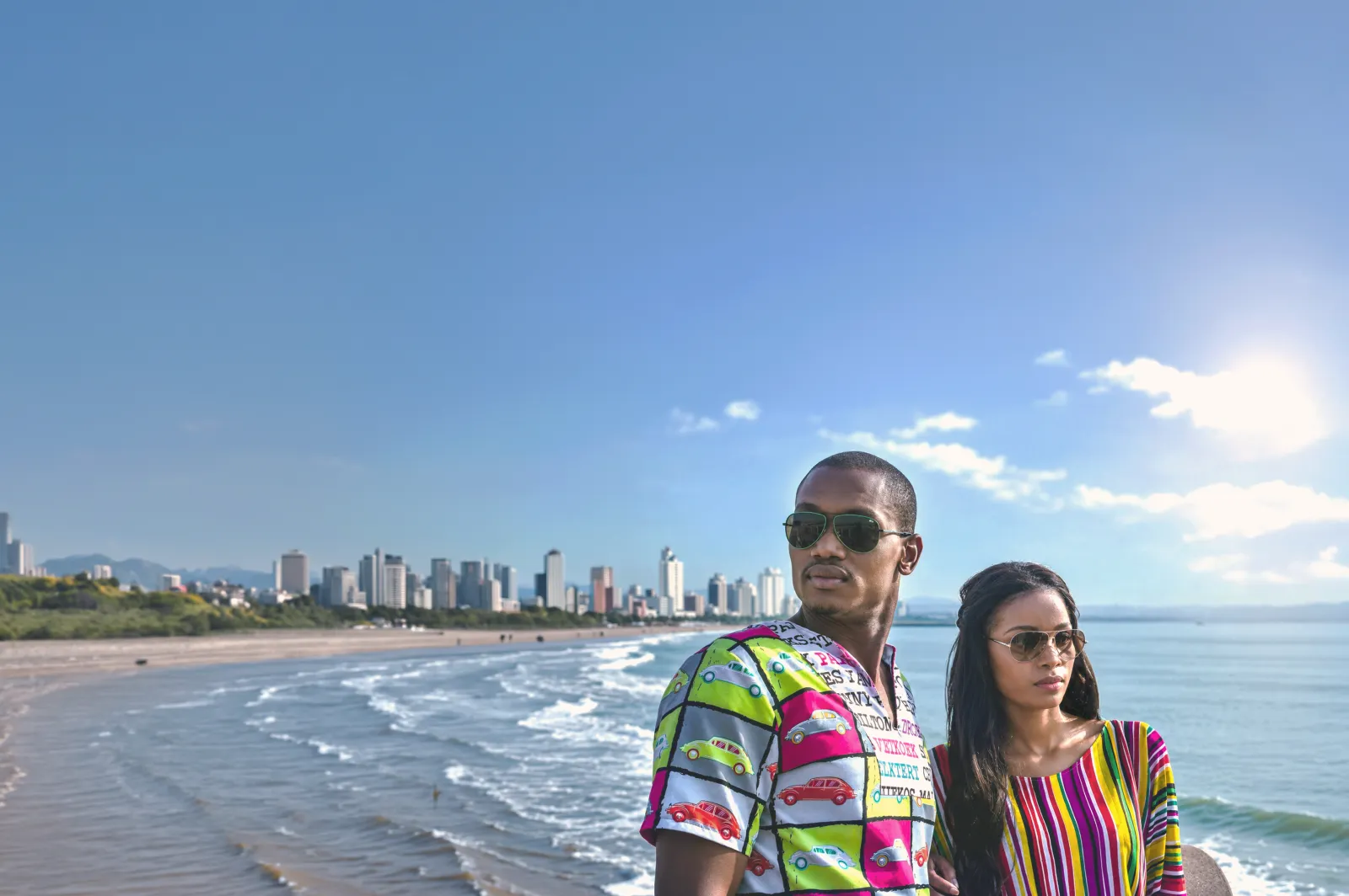 Two event attendees in colourful outfits beside a South African beachfront skyline